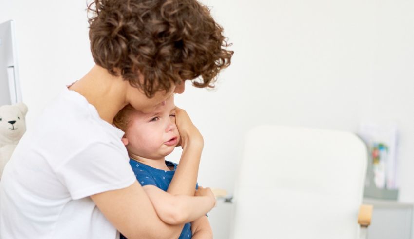 A woman is holding a crying child in front of a teddy bear.