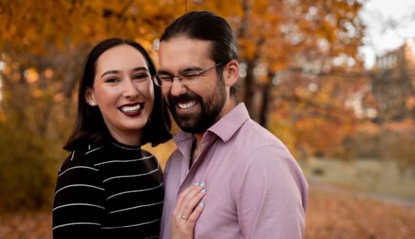 A couple smiles in front of a tree in a park.