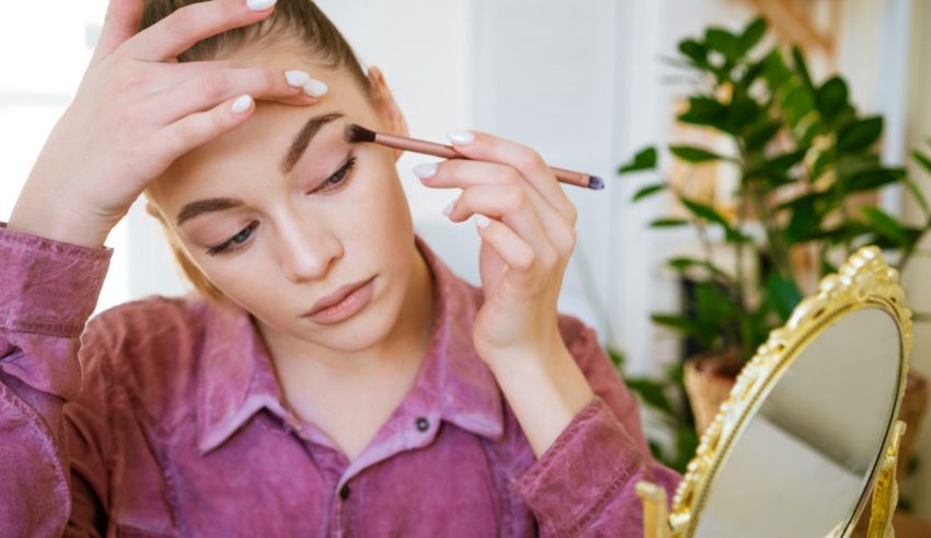 A woman is putting makeup on her eyebrows in front of a mirror.