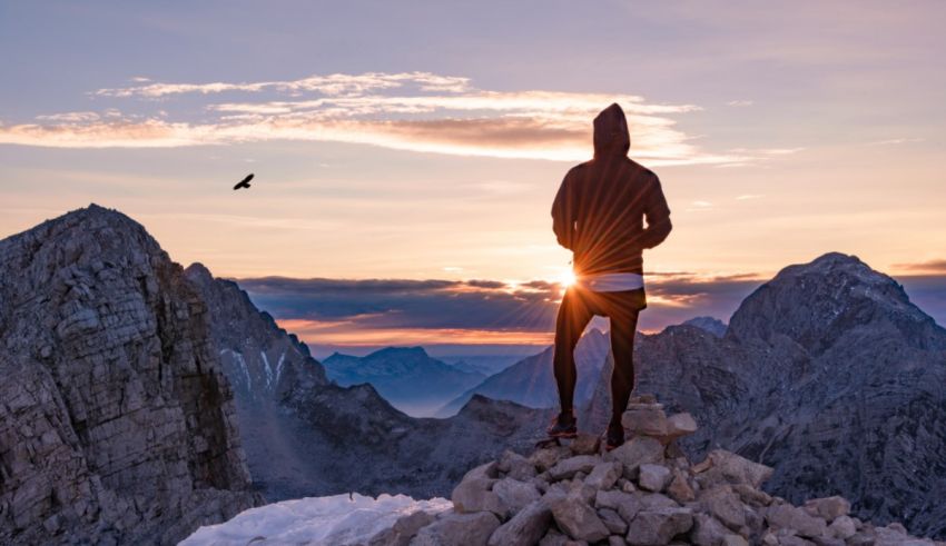 A man is standing on top of a mountain at sunset.