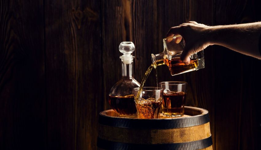 A man pouring whiskey into glasses on a wooden barrel.