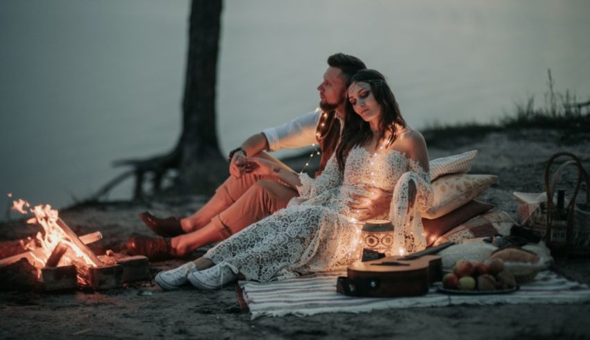 A couple sits around a campfire at dusk.
