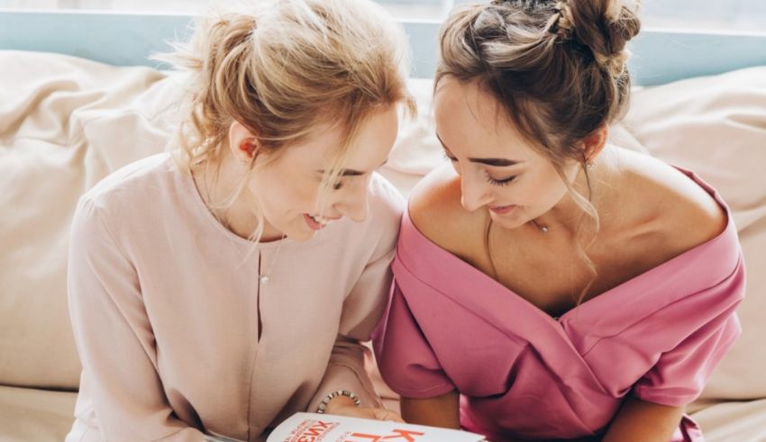 Two women sitting on a couch looking at a book.