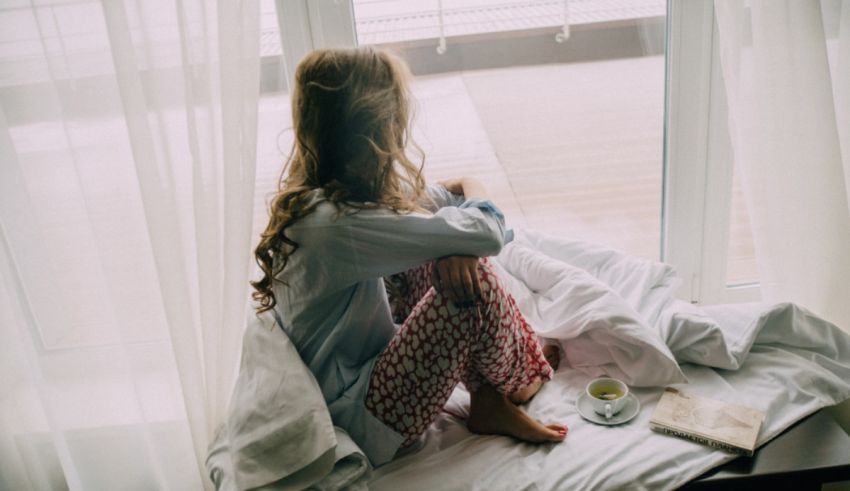 A young woman sitting on a bed with a cup of coffee.