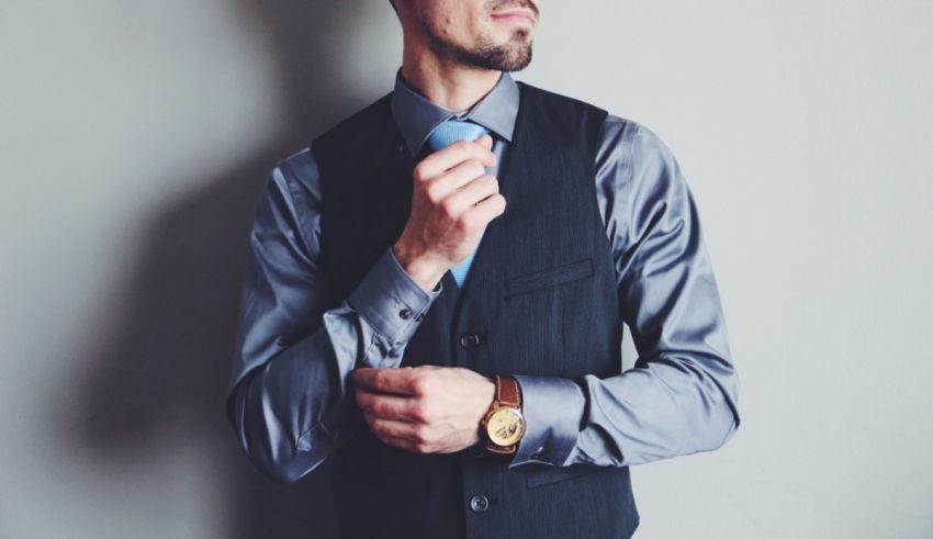 A man is adjusting his tie on a gray wall.