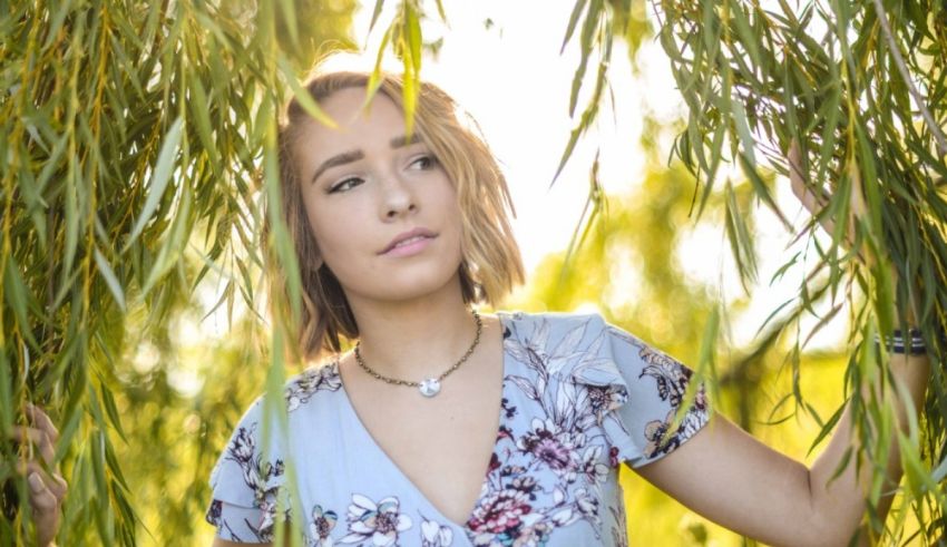 A young woman is hiding behind a willow tree.