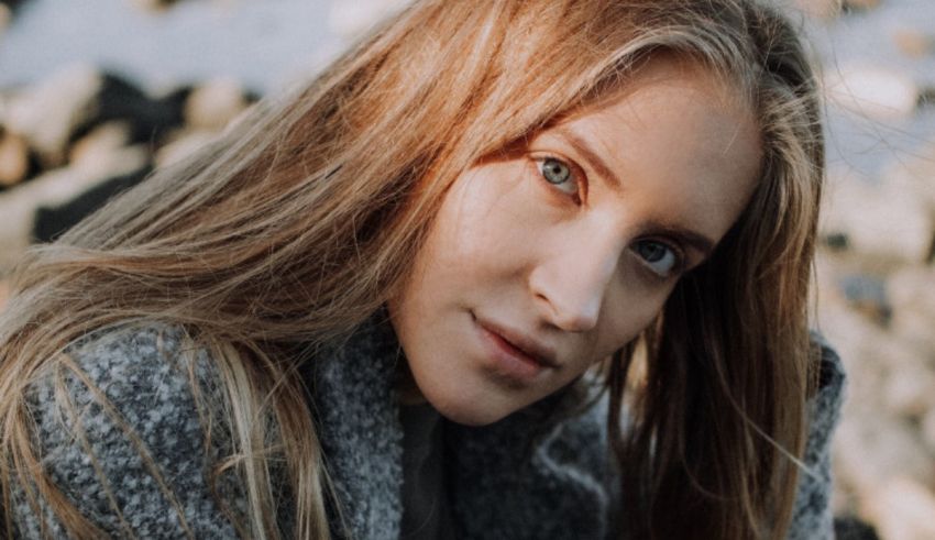 A woman with long blonde hair is posing in front of rocks.