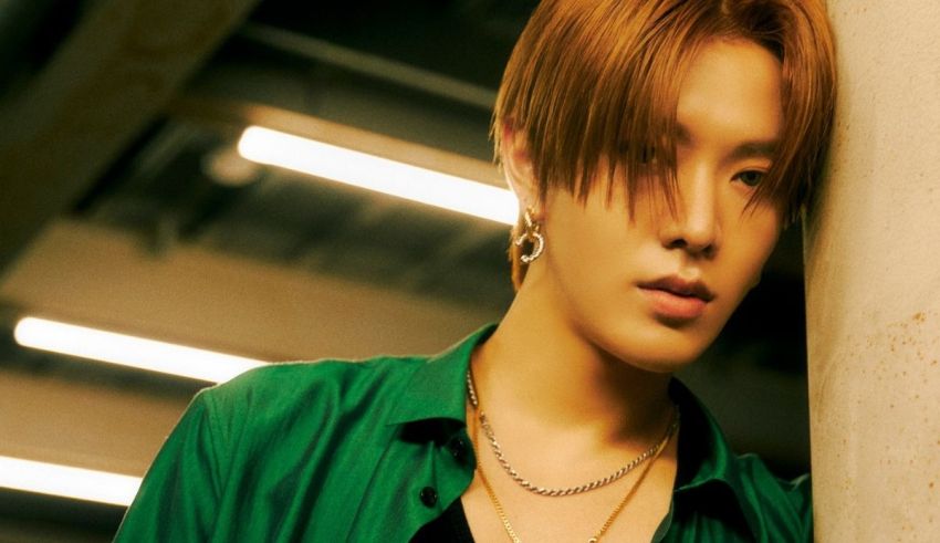 A young man in a green shirt leaning against a wall.