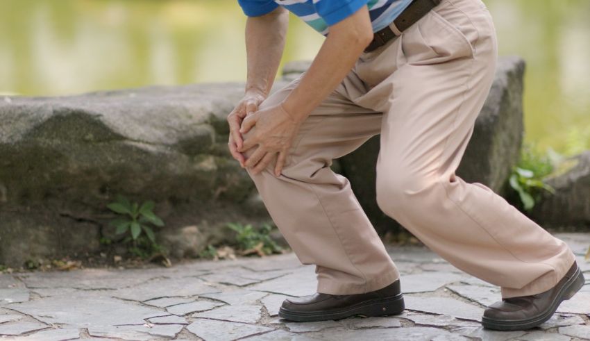 A man in a tan shirt is holding his knee.