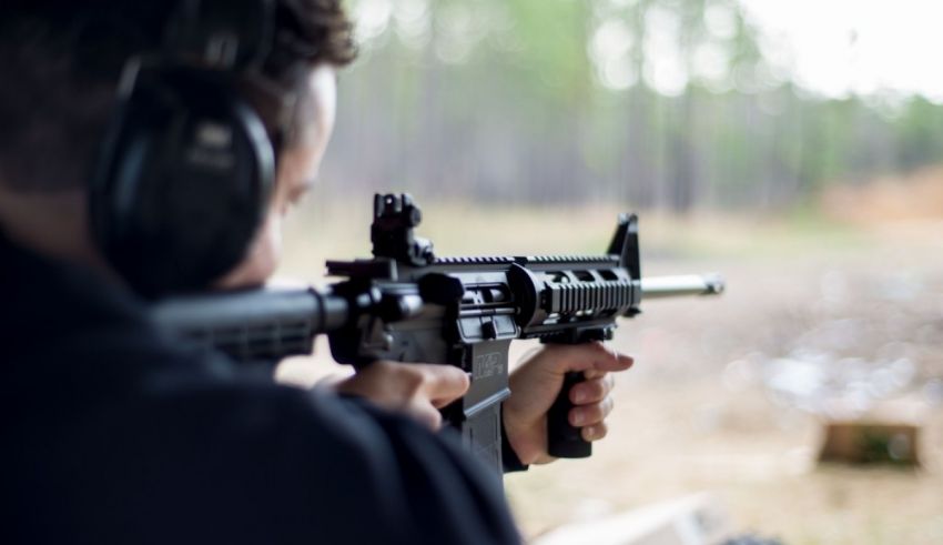 A man is shooting a rifle in a wooded area.