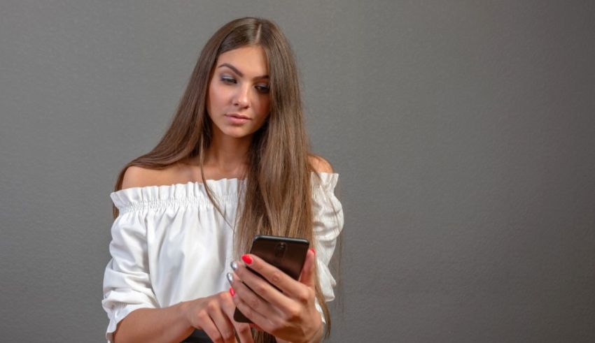 A young woman looking at her phone on a gray background.