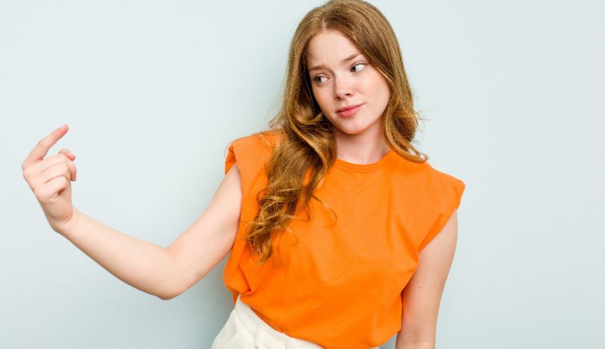 A young woman in an orange shirt pointing to her finger.