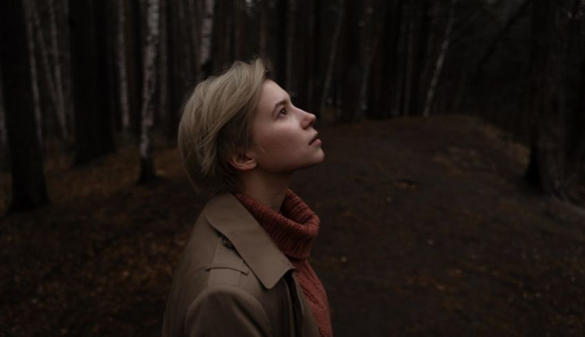 A woman in a trench coat standing in a wooded area.