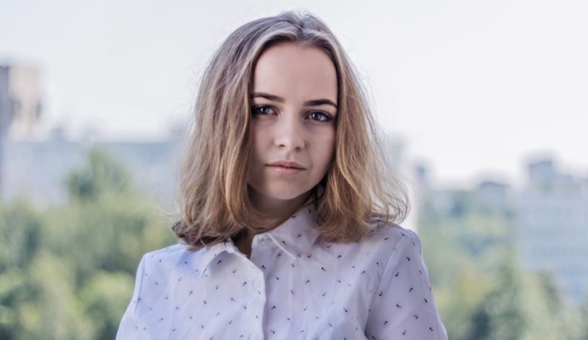 A young woman in a white shirt is standing in front of a city.