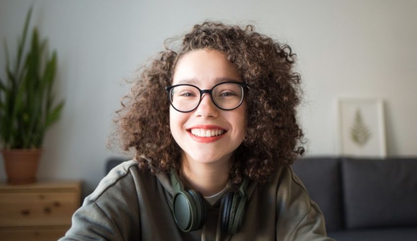 A young girl wearing glasses and headphones is sitting on a couch.