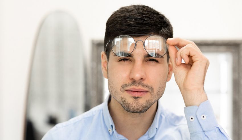 A man is looking at his glasses in a mirror.
