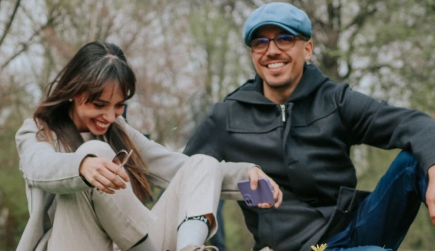 A man and woman are sitting on the ground with a cell phone in their hands.