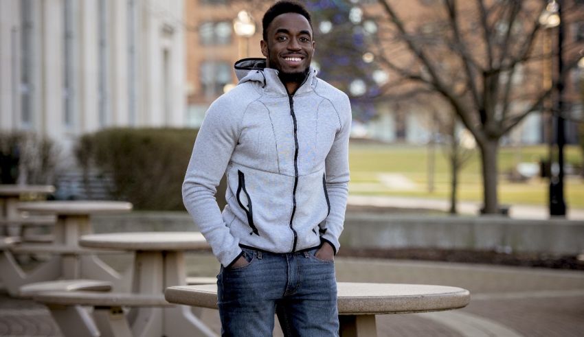 A young man in jeans and a hoodie standing in front of a bench.