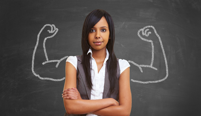 A black woman standing in front of a chalkboard with her arms crossed.