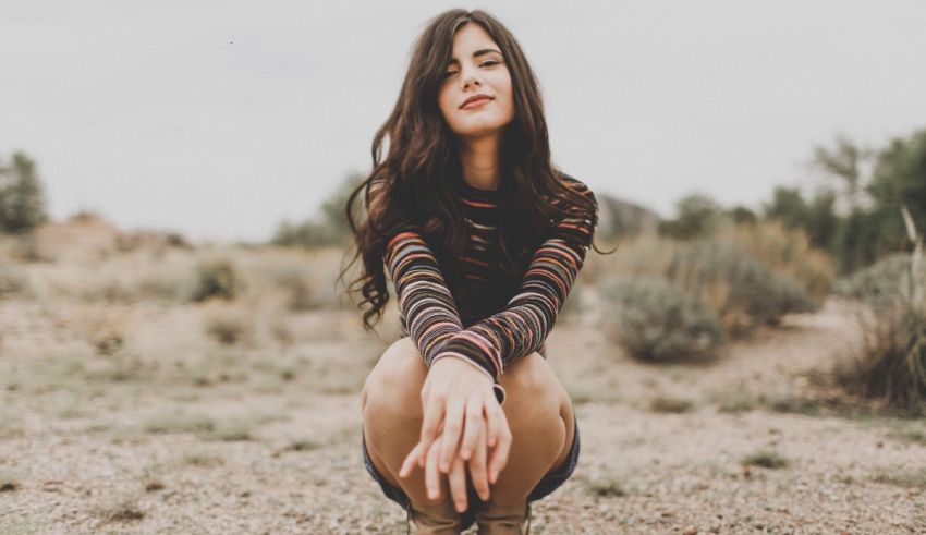 A young woman crouching down in a field.