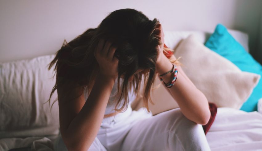 A woman sitting on a bed with her hands on her head.