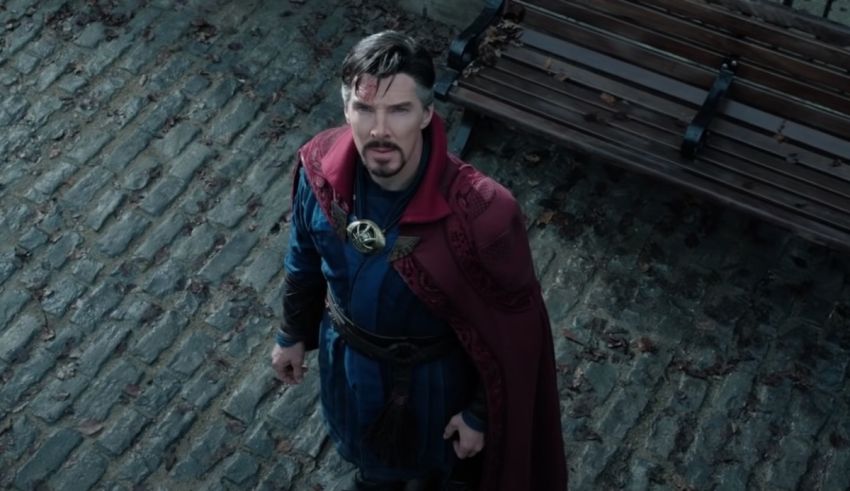 A man in a red cape standing next to a bench.