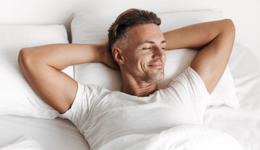 A man is laying in bed with his hands on his head.