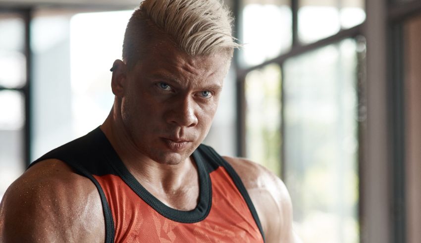 A man in a tank top is posing in a gym.