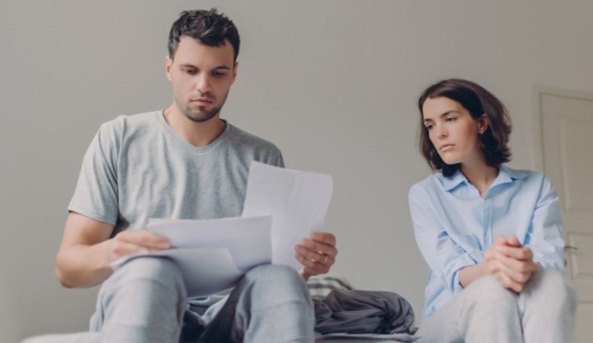 A man and woman sitting on a bed with papers in front of them.