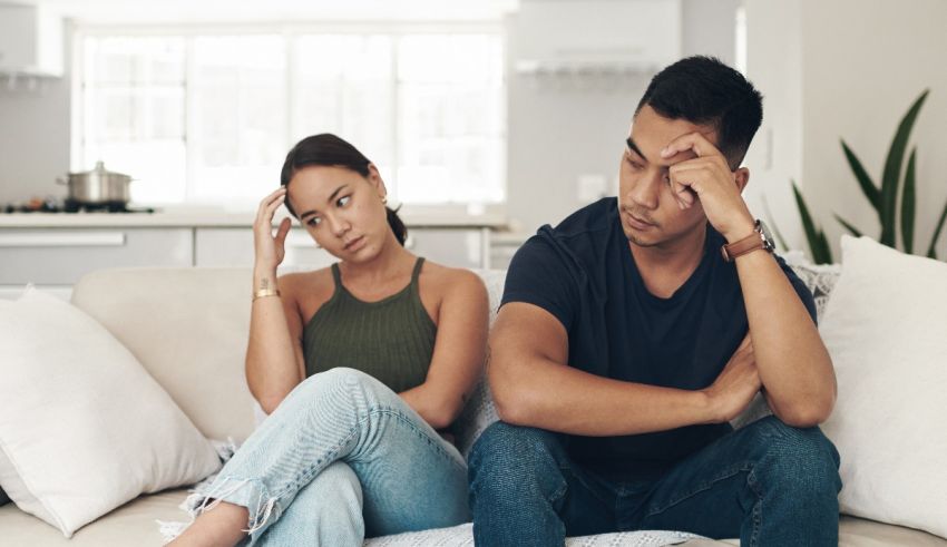 A man and woman sitting on a couch with their hands on their heads.