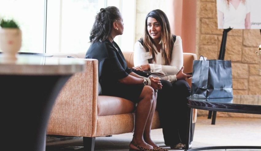 Two women talking on a couch in a lobby.