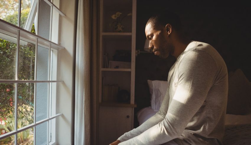 A man looking out of a window in his bedroom.