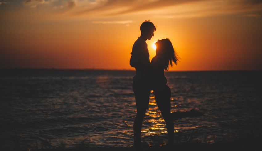 A man and woman standing on the beach at sunset.