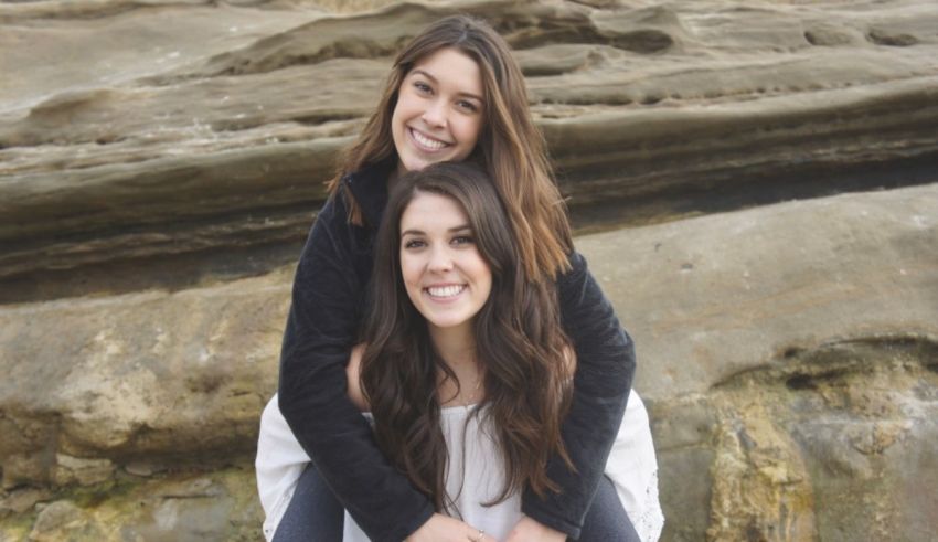Two girls hugging in front of a rocky beach.