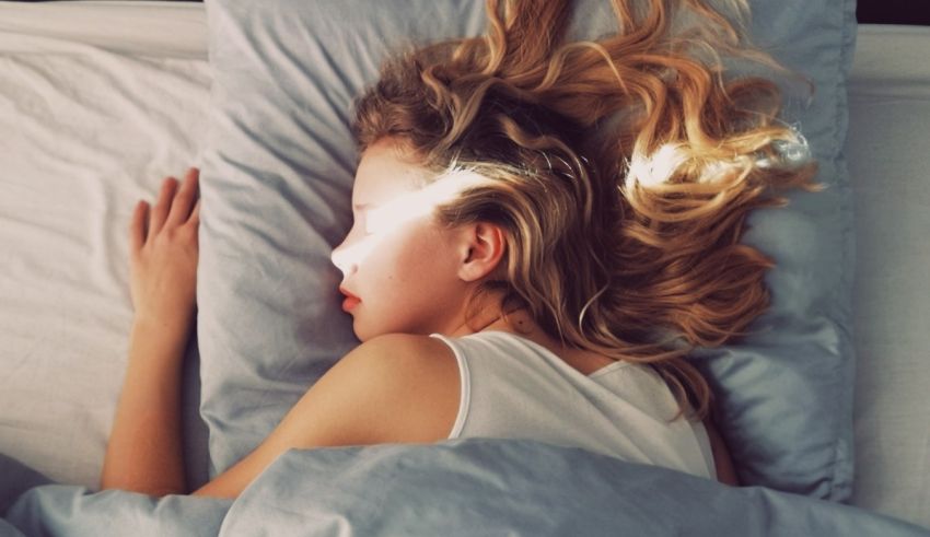 A young woman sleeping in bed with her hair blowing in the wind.