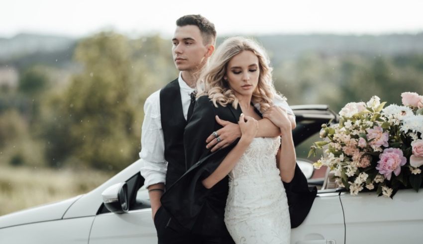 A bride and groom posing in front of a car.