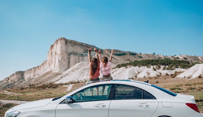 Two women standing on top of a mercedes car.