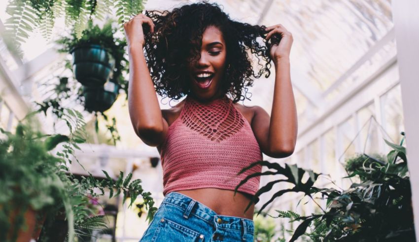 A young black woman with curly hair standing in a greenhouse.