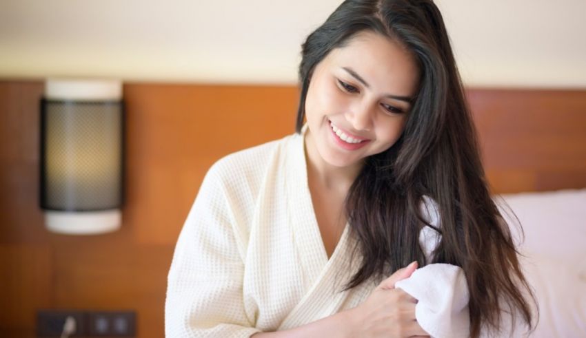 A woman in a white robe is smiling while sitting on a bed.