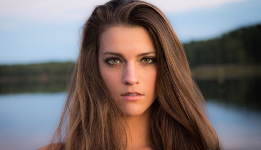 A young woman with long brown hair in front of a lake.