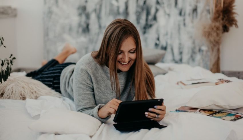 A young woman laying on a bed and using a tablet.