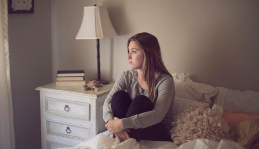 A young woman sitting on a bed in a bedroom.