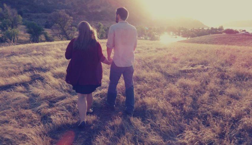 A couple walking through a field at sunset.