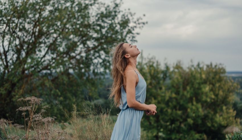 A young woman in a blue dress is standing in a field.