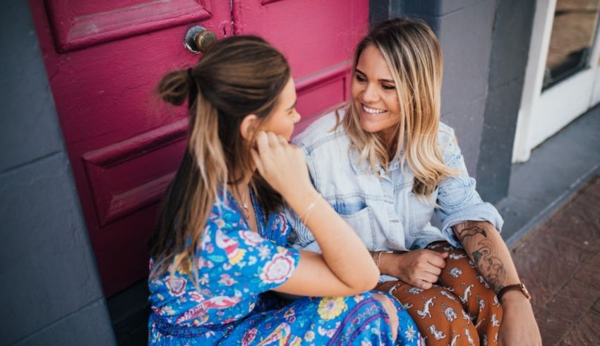 Two women sitting in front of a pink door.