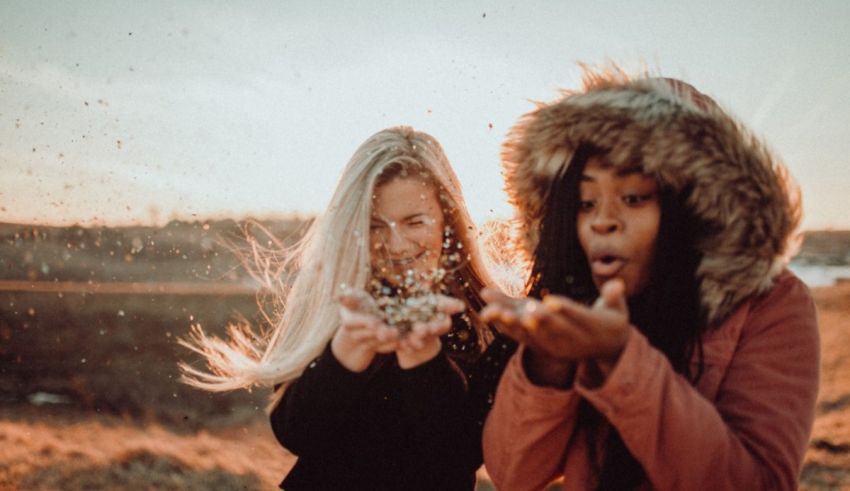Two women in a field blowing sand into each other's faces.