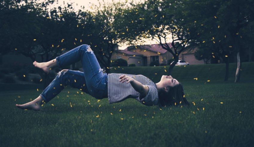 A woman laying in the grass with fireflies flying around her.