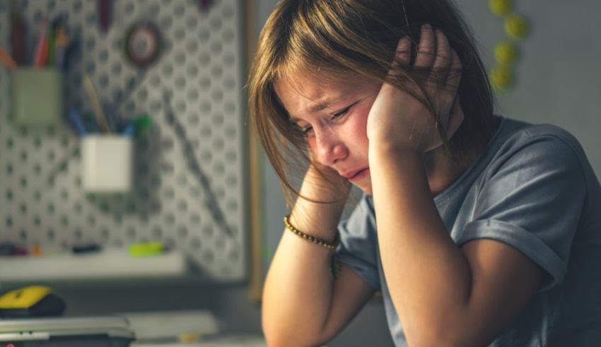 A girl is sitting at a desk with her hands on her head.