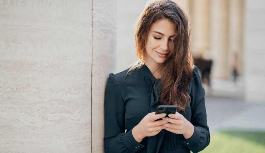 A young woman is leaning against a column while using her cell phone.
