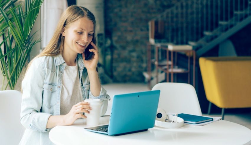 A woman is talking on the phone while sitting at a table with a laptop.